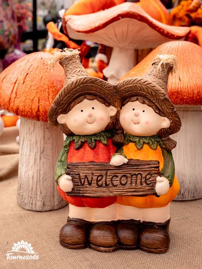 Figurines d'automne souriantes tenant une pancarte 'Welcome' devant des champignons décoratifs.
